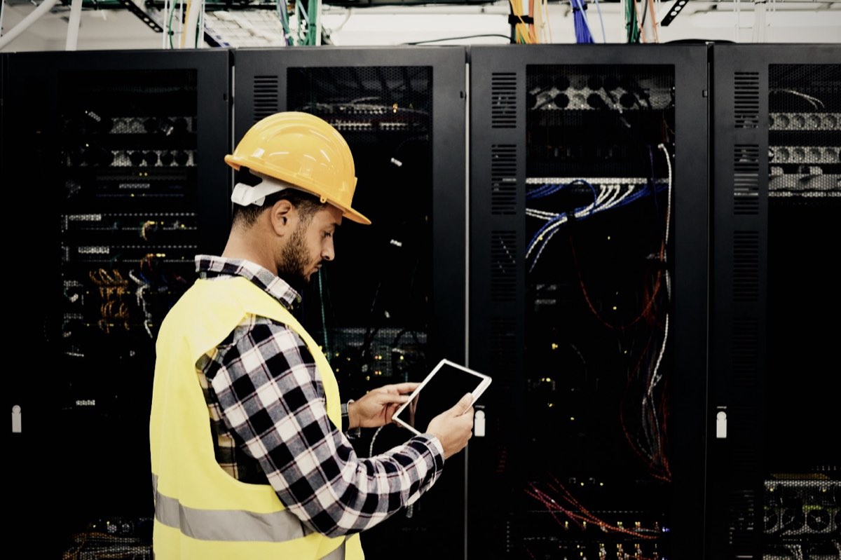 Worker in a hard hat using a tablet in a server room