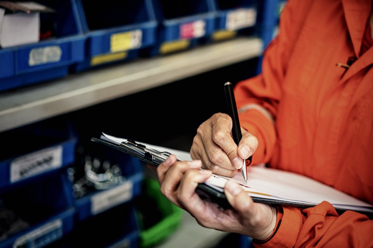 Inspector in hi-vis completing an audit checklist among parts bins