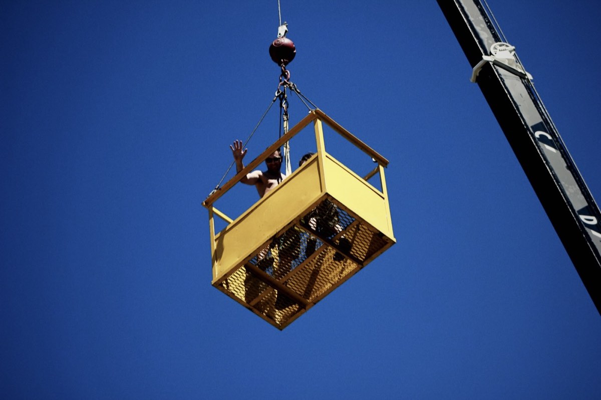 Workers in a personnel basket lifted by a crane against a blue sky